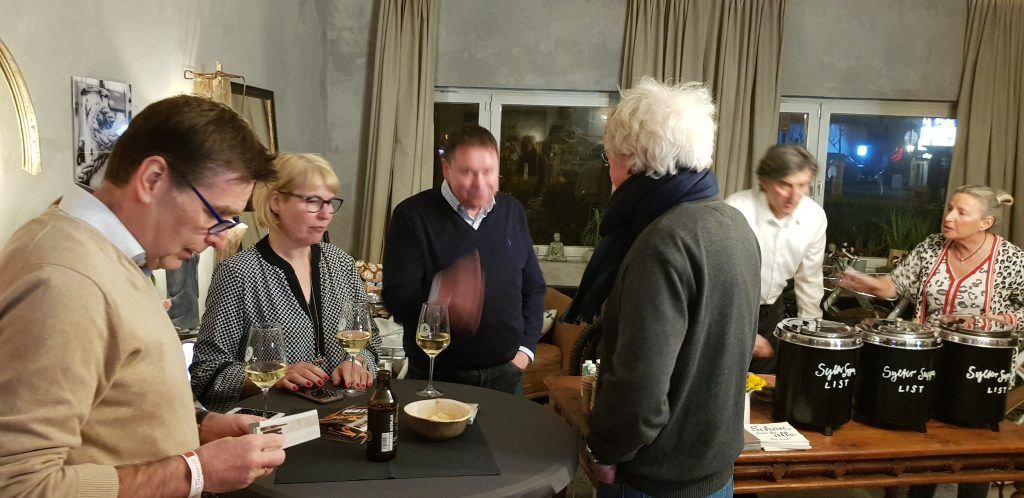 Eine Gruppe von Menschen steht mit Weingläsern um einen Tisch.