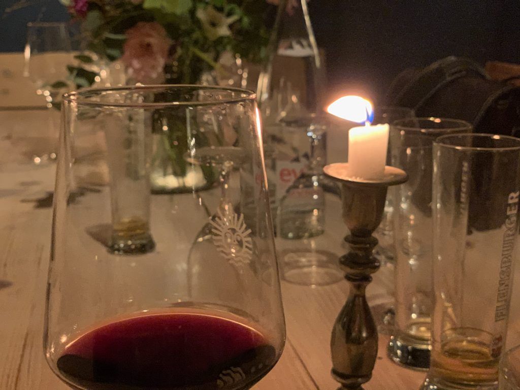 Ein Glas Wein neben einer Kerze auf einem Tisch.