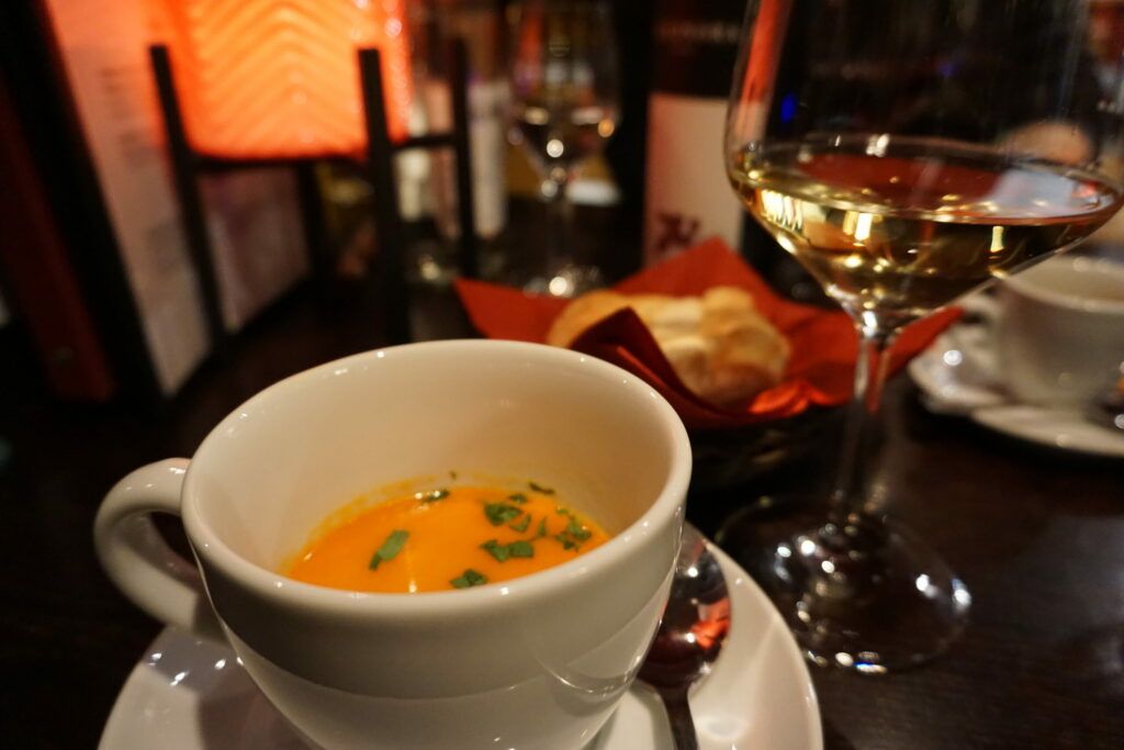 Eine Tasse Suppe auf einem Tisch neben einem Glas Wein.