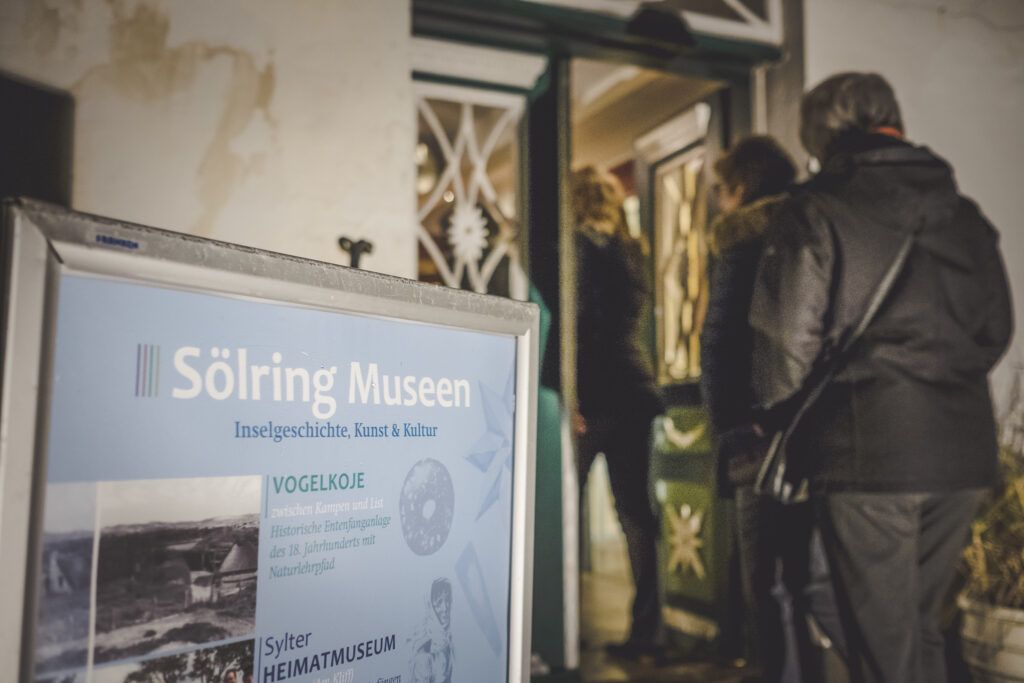 Eine Gruppe von Menschen steht vor einem Schild mit der Aufschrift Sölring Museum.