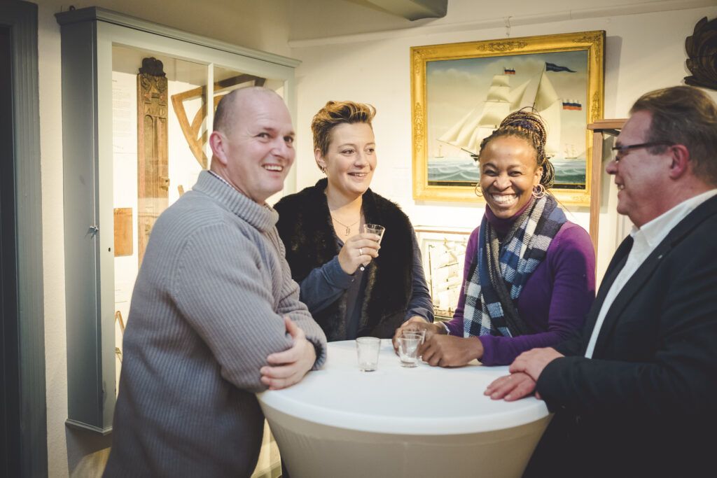 Vier Menschen lächeln an einem Tisch in einer Kunstgalerie.