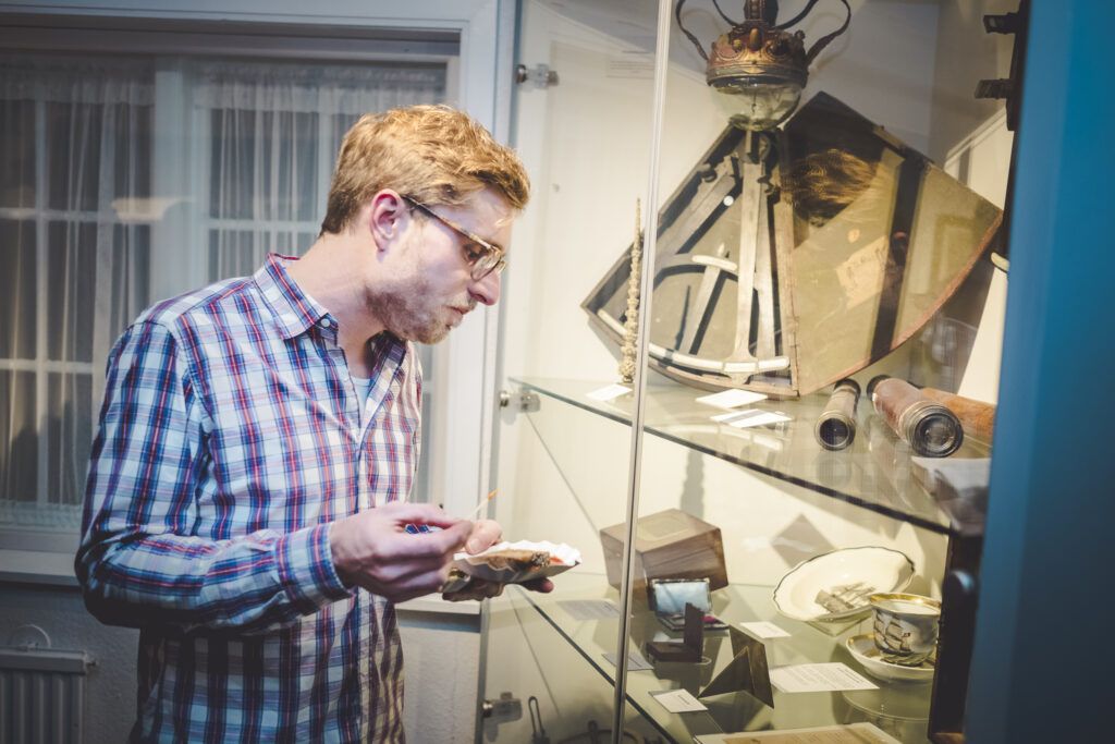 Ein Mann in einem karierten Hemd betrachtet Gegenstände in einer Glasvitrine.