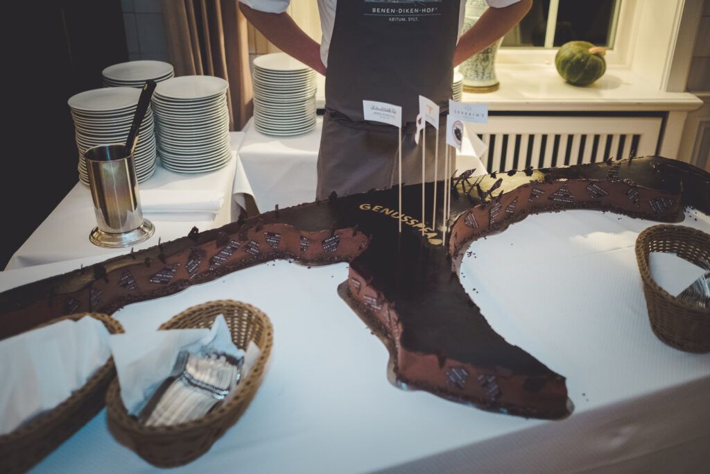 Ein Mann mit Schürze steht vor einem Schokoladenkuchen in Sylt-Form
