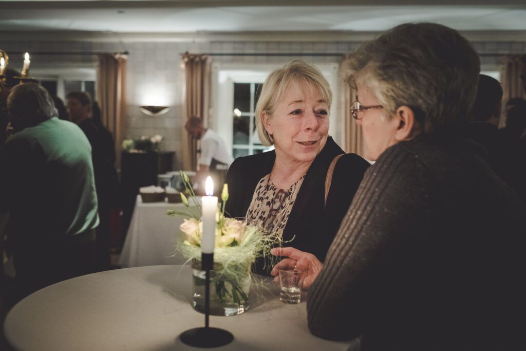 Zwei ältere Frauen unterhalten sich an einem Tisch auf einer Party.