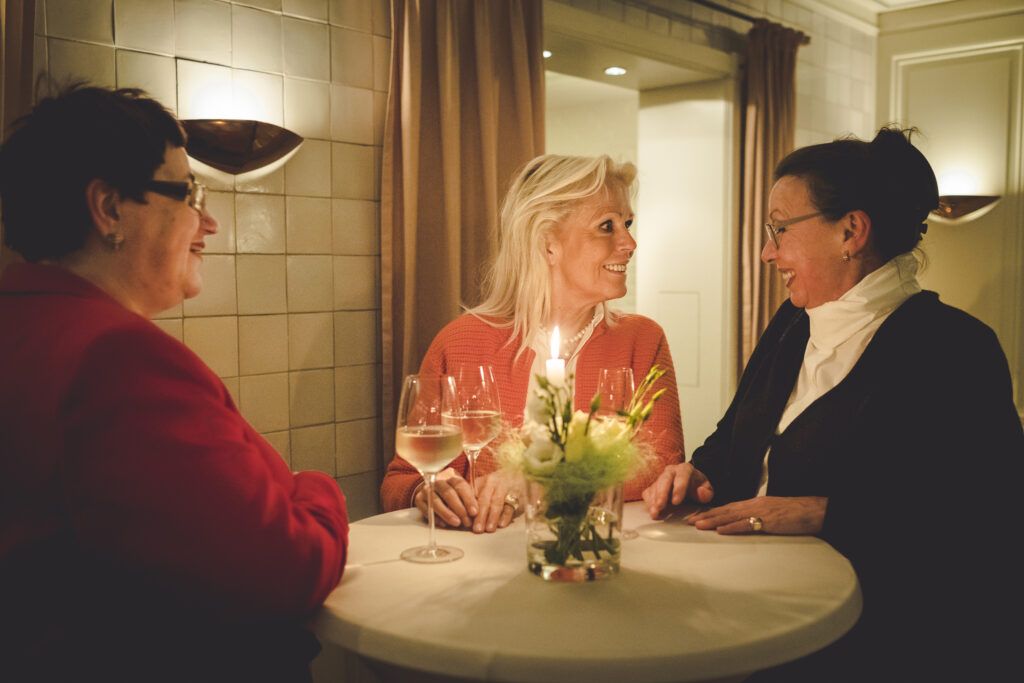 Drei Frauen sitzen mit Weingläsern an einem Tisch.