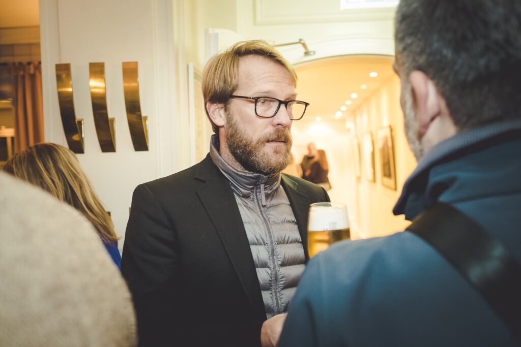 Ein Mann mit Brille spricht bei einer Veranstaltung mit einem anderen Mann.