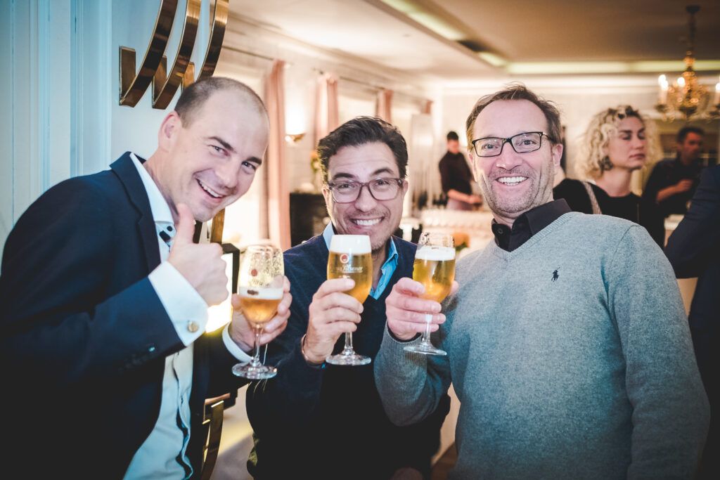 Drei Männer halten Gläser Bier auf einer Party.
