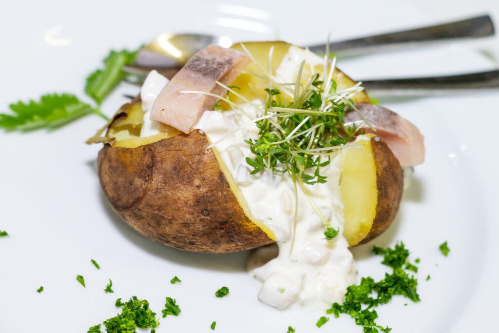 Ein weißer Teller mit einer Kartoffel, garniert mit Sauerrahm und Kräutern.