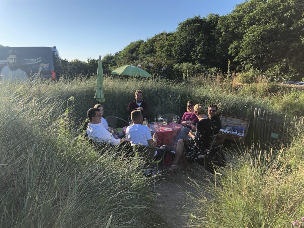 Eine Gruppe von Menschen sitzt um einen Tisch im hohen Gras.