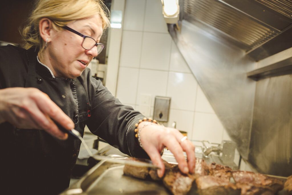 Eine Frau bereitet in einer Küche ein Steak zu.