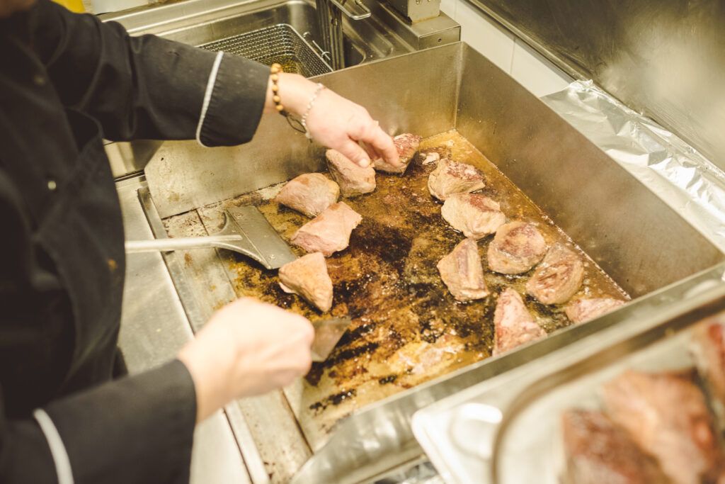 Ein Koch bereitet in einer Küche Fleisch auf einer Grillplatte zu.
